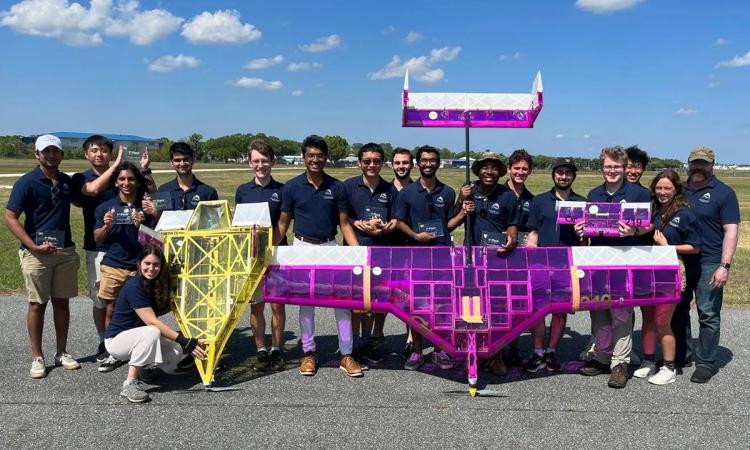 The Design Build Fly Teams with their two aircraft: A small yellow craft called Buzzgiorno and a larger magenta-colored craft called Incombuzztible.