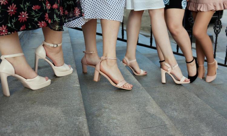 Five pairs of feet in high heels standing on steps.
