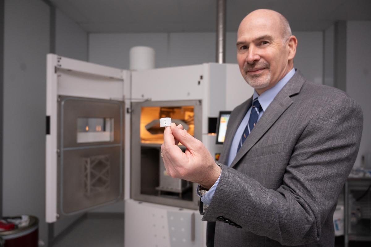 Scott Hollister stands in front of a 3D printer holding up a 3D-printed airway splint