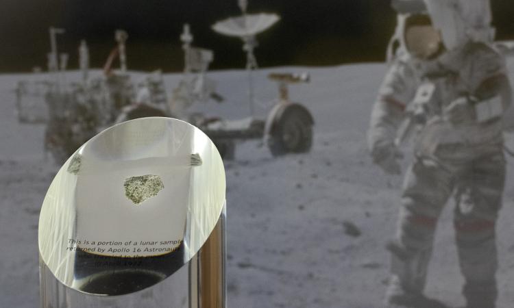 Closeup of a lunar sample suspended in an acrylic cylinder with an image in the background of astronaut John Young on the moon. (Photo: Candler Hobbs)