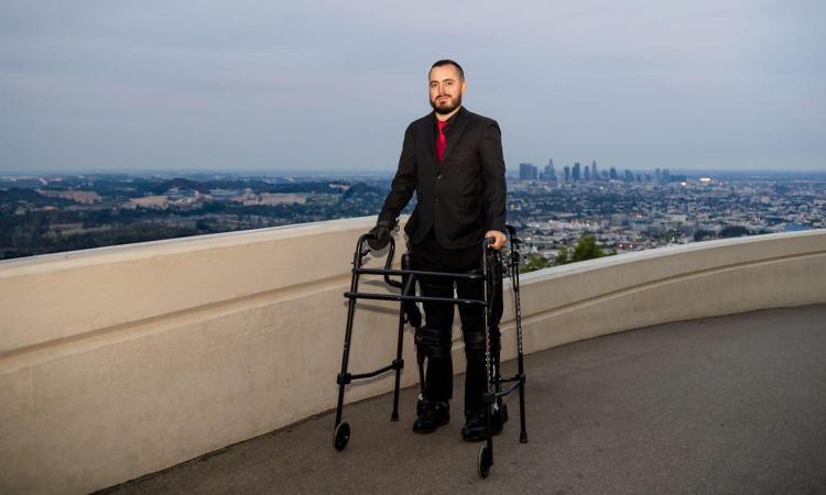 Ignacio Montoya stands with a walker in front of the Los Angeles skyline.