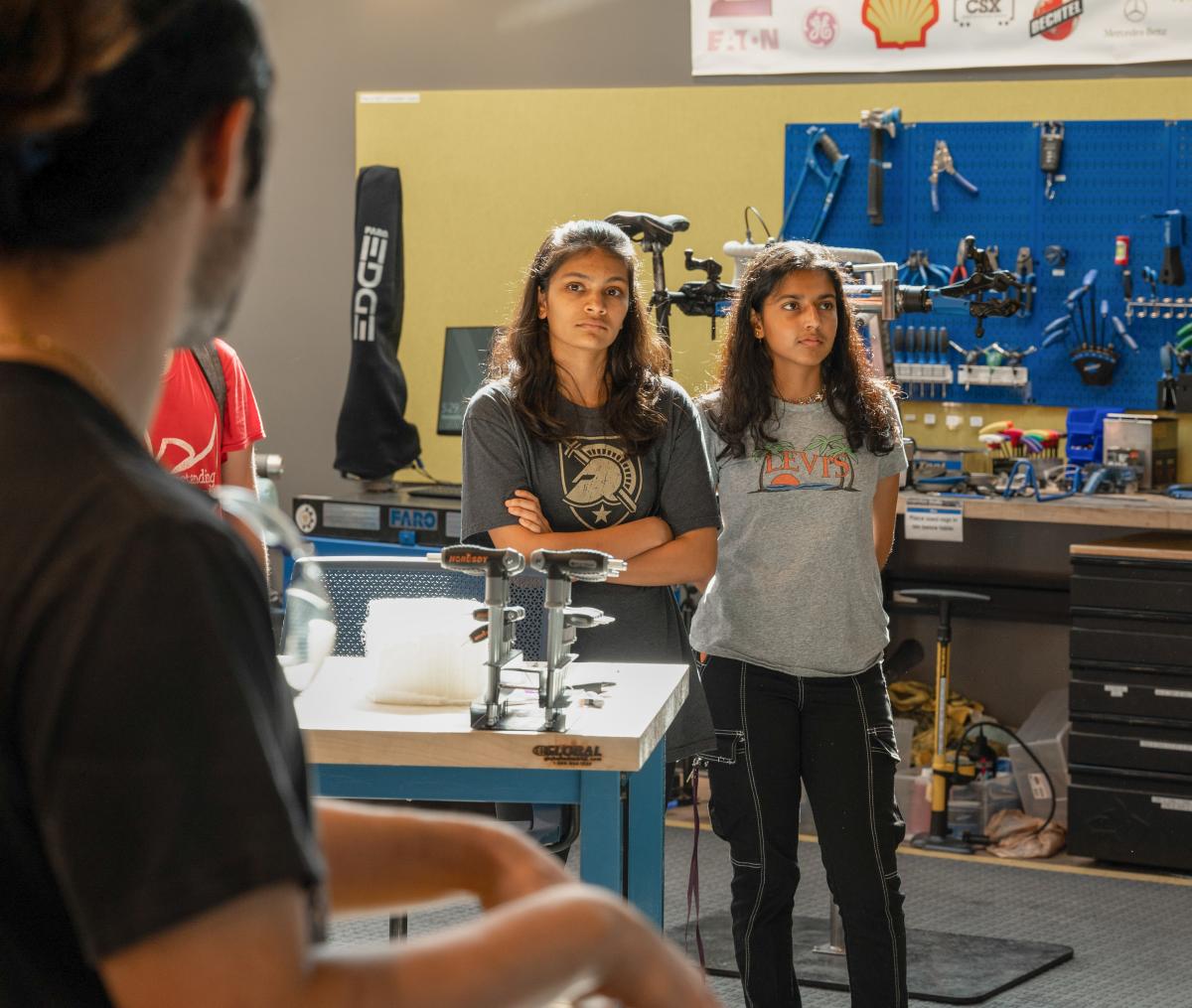 two female students listening to someone out of frame speaking. all are standing in lab