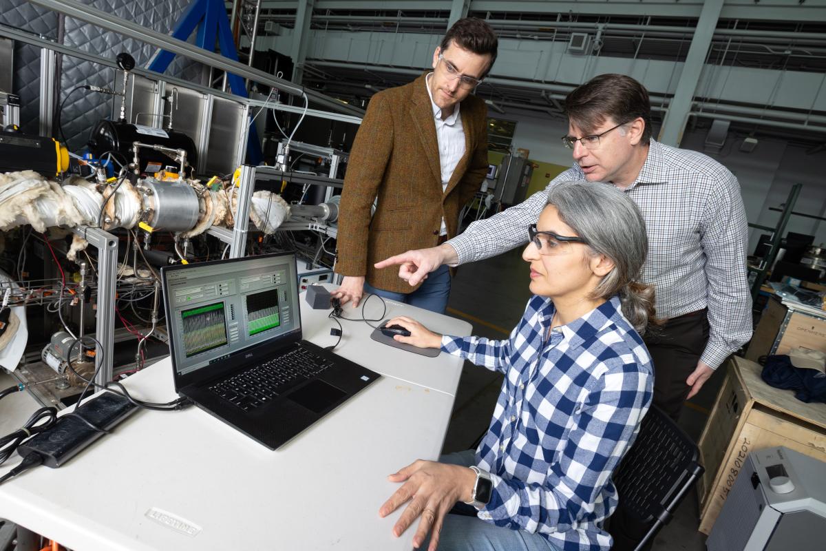 Three people in a lab look at a laptop screen in front of a direct air capture system